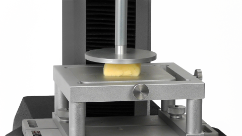 A hard cheese variety 1 inch cube texture test sample being compressed to calculate its springiness property